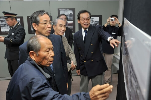 日野宿のパノラマ写真を前に松本保さん、加島教育長、真野保さん